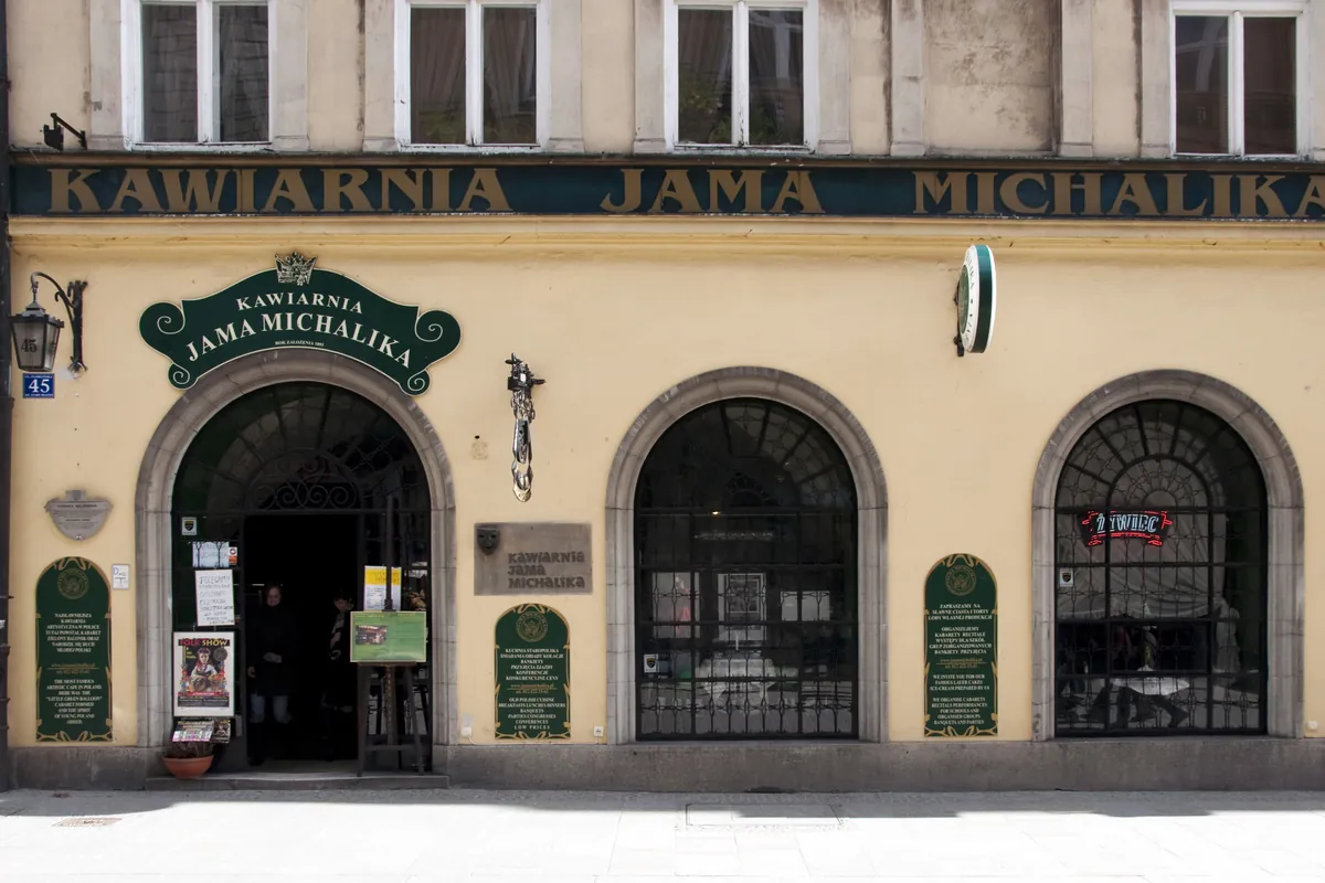The yellow front of Jama Michalika on Floriańska Street, with a name board over an arched doorway and two arched barred windows.