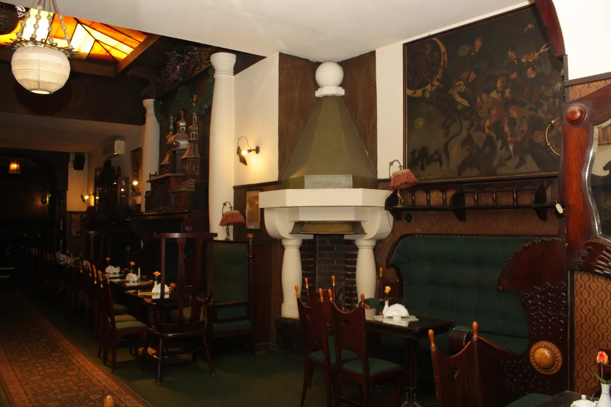 A white hooded fireplace beside a green leather bench, with a large dark painting above it.